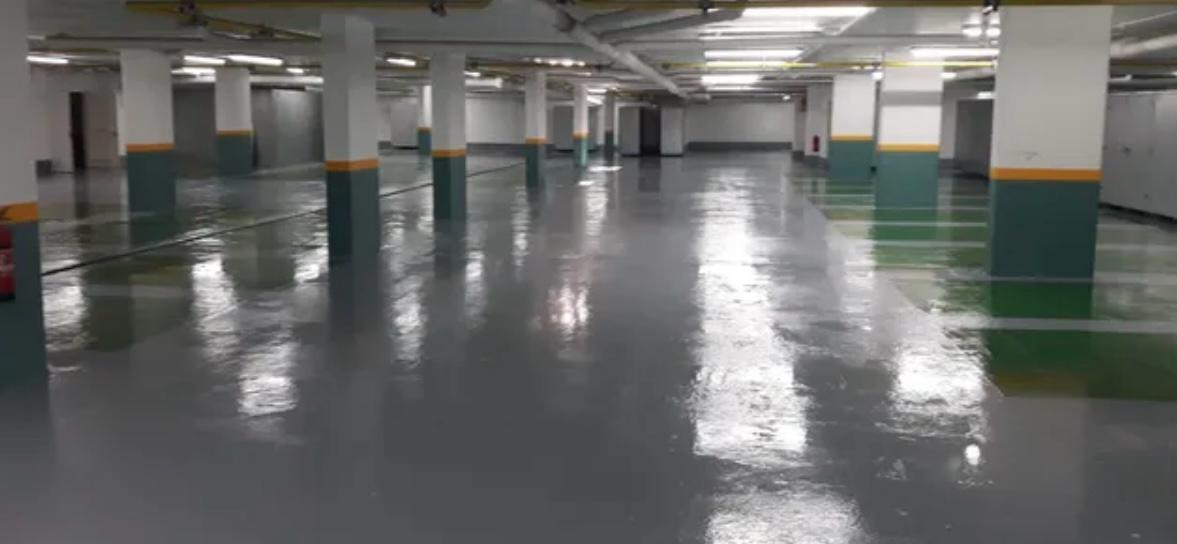 Empty indoor parking garage with polished concrete floor, lined with white support columns featuring a yellow and green stripe near the base.